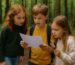 Drei Kinder im Wald rätseln gemeinsam mit einer Karte und Lupe in der Hand – Naturabenteuer pur