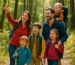 Eine fünfköpfige Familie wandert fröhlich auf einem Waldweg – die Eltern mit Rucksack und drei lachende Kinder mit Wanderstöcken genießen die Natur. wandern mit kindern